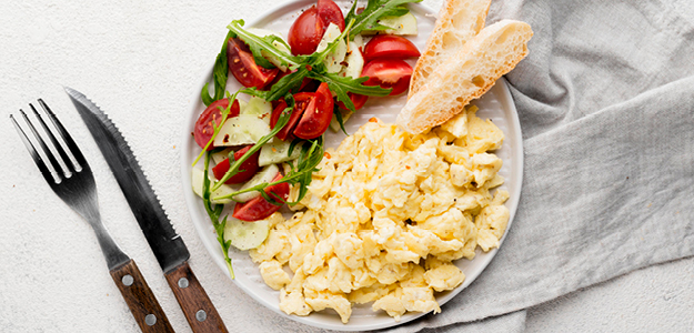 A breakfast dish with eggs, tomatoes, rocket and bread